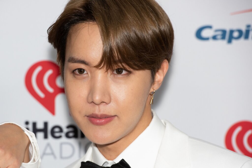 Homem com cabelo curto com franja castanho escuro, usando terno branco, camisa branca e gravata borboleta preta