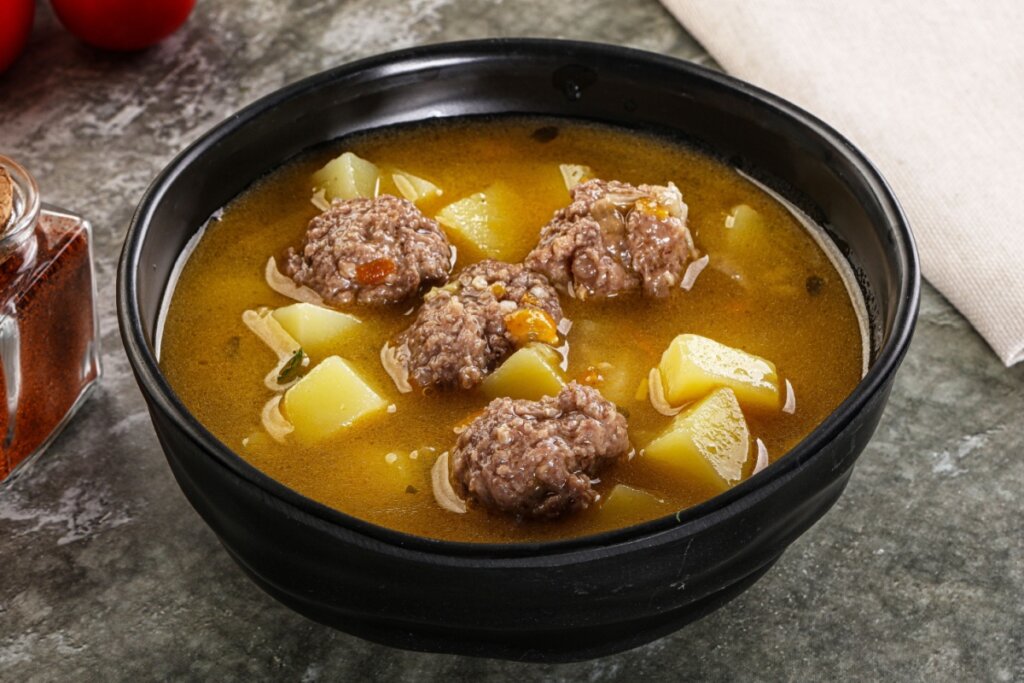 Tigela preta funda com sopa de almôndegas e batata
