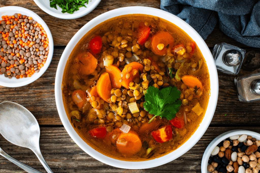 Sopa de lentilha com cenoura e tomate servida em tigela branca em cima de mesa de madeira