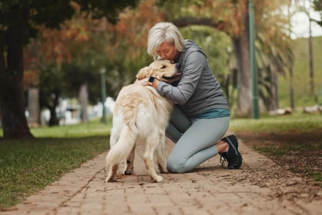 Mulher agachada dando beijo na cabeça de um cachorro em um parque