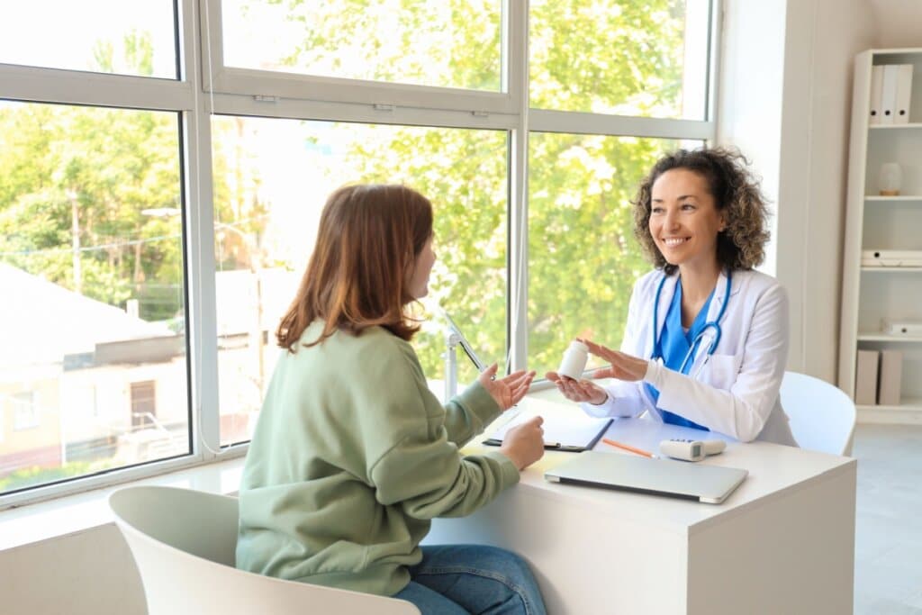 médica e paciente sentadas uma de frente para a outra. médica segura frasco de remédio e sorri.