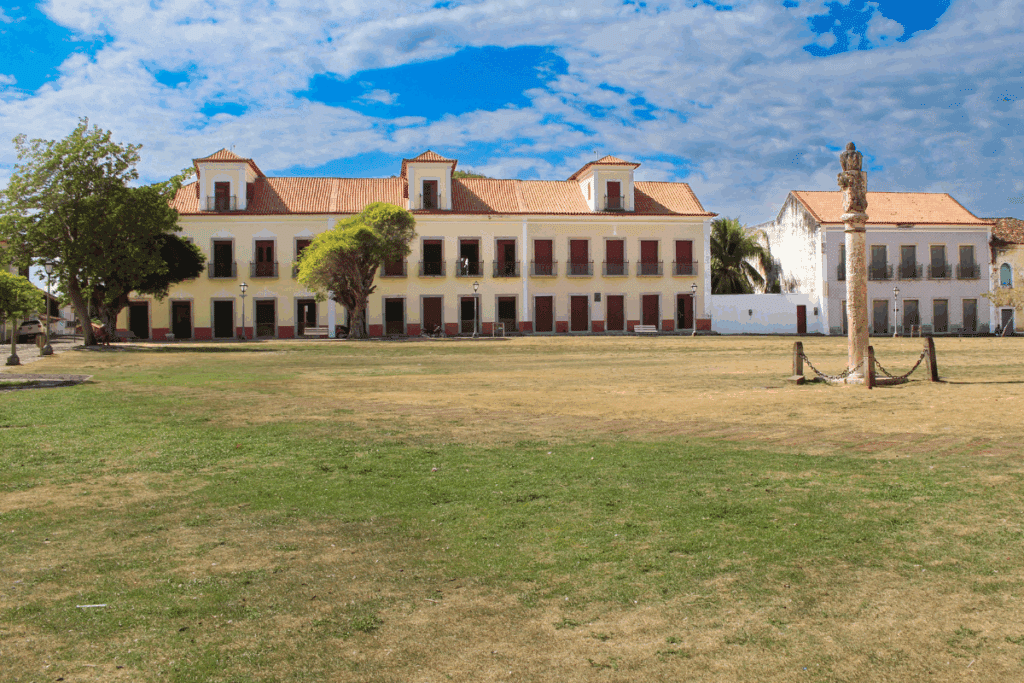 Praça da Matriz (Largo de São Matias) em Alcântara (MA), destacando o Pelourinho colonial em primeiro plano e casarios históricos ao fundo, sob céu azul com nuvens